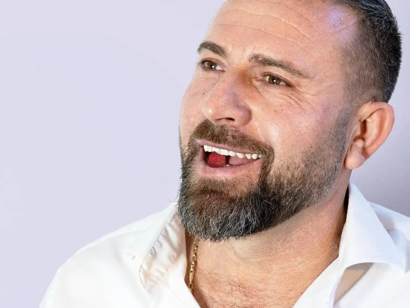 A man with a cbd gummy in his mouth (purple background)